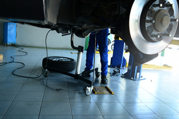 the legs of a mechanic in blue uniform and safety shoes  working under the car the  black wheel...