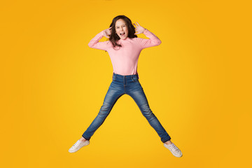 Fototapeta na wymiar Excited girl jumping and shouting over yellow background