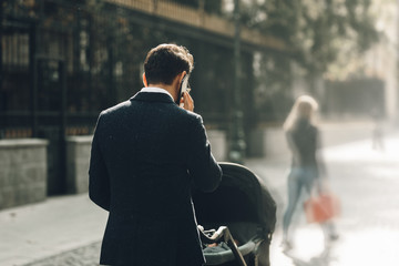 businessman parent outside with stroller on the street dressed in suit, looking elegant and fashion talking at the phone