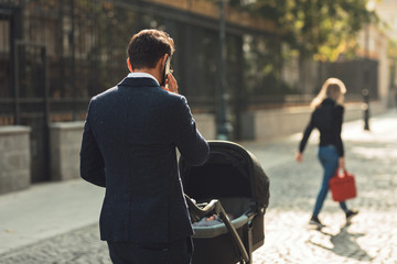 businessman father looking elegant and talking at the phone outside walking with his daughter stroller carriage