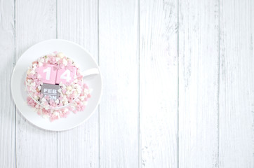 Pink square wood with white numbers 1 and 4.Gray square wood with white letters FEB.February 14 Valentine's Day.White coffee cup on wooden floor.Many small hearts, white and pink.