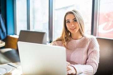 Beautiful young woman using laptop at cafe look at camera in cafe