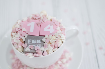 Pink square wood with white numbers 1 and 4.Gray square wood with white letters FEB.February 14 Valentine's Day.White coffee cup on wooden floor.Many small hearts, white and pink.