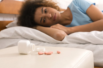 Fototapeta na wymiar Sick woman looking at pills, lying on bed