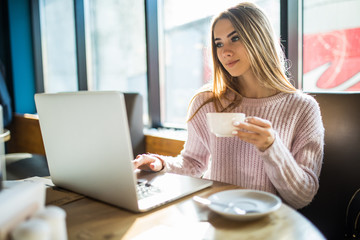 Young woman drinking coffee or tea and using tablet computer in a coffee shop
