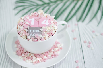 Pink square wood with white numbers 1 and 4.Gray square wood with white letters FEB.February 14 Valentine's Day.White coffee cup on wooden floor.Many small hearts, white and pink.