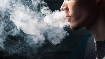 A young man releases a cloud of steam . Alternative to Smoking. Electronic cigarette