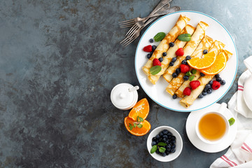 Sweet pancakes wrapped with fresh berries, crepes with blueberry and raspberry on breakfast, top view