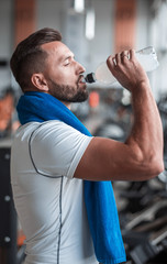 Fototapeta na wymiar Young adult man drinking bottle of water on trreadmill in gym.