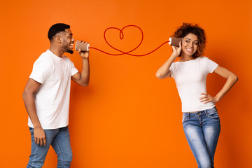 Young black couple with can phone on orange background