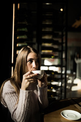 Portrait of young woman drinking coffee at table in cafe