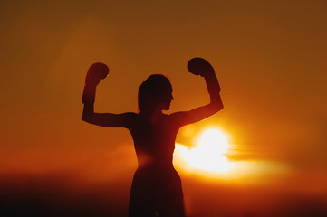 Silhouette of the girl in boxing gloves at sunset.