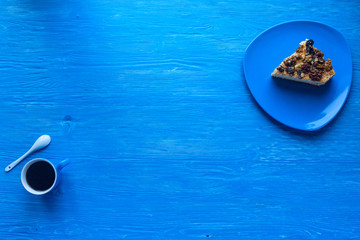 Sponge cake with walnuts, next to a cup of coffee on a wooden background, photographed from above.