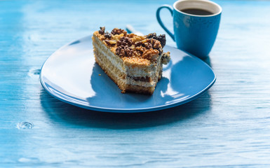 Sponge cake with walnuts, near a cup of coffee on wooden background.