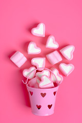marshmallows  heart shaped candies spilled from a pink iron bucketon a pink background Happy Valentine's Day Flat lay Top view