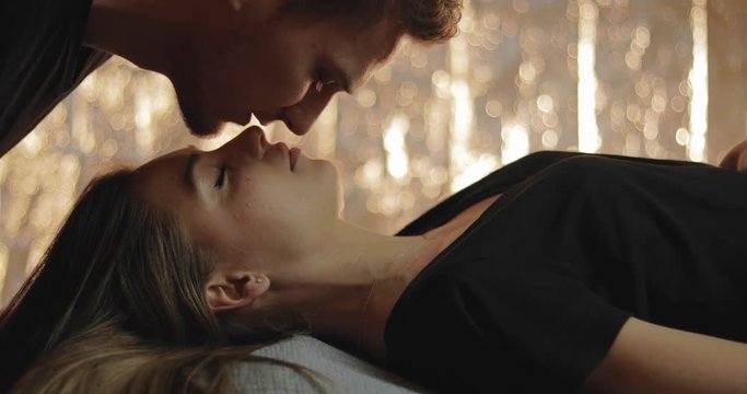 A sweet moment as a young woman sleeps as her boyfriend gives her gentle upside down kisses to wake her