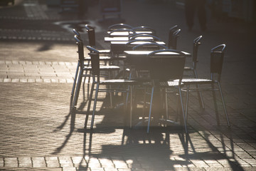 empty set of tables and chairs outside a cafe glistening in the early morning sun