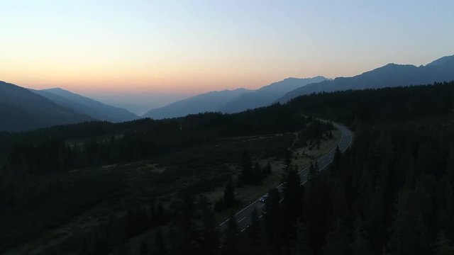 Countryside highway in-between pine forest of Gerlos Pass, at golden hour sunrise with a car cruising by
(drone shot)
