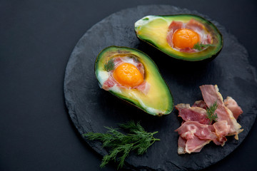 tasty baked avocado with an egg on a black background