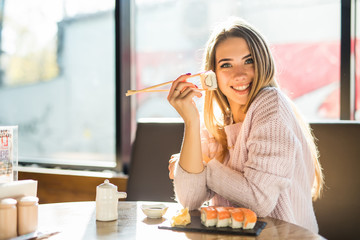 Young blond woman eating with stick sushi in an Asian restaurant