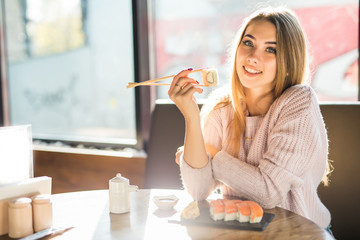 Young blond woman eating with stick sushi in an Asian restaurant