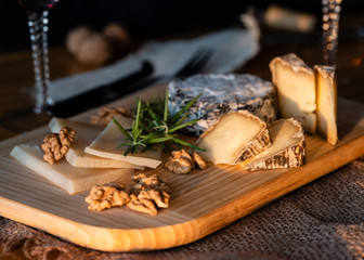 Some kinds of the blue cheeses with halves of the walnuts and rosemary, two glasses with red wines, knife and fork on the wooden desk