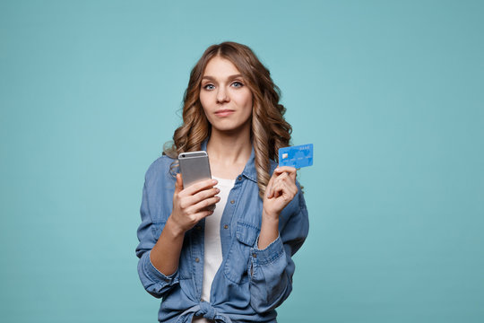 Image of excited young lady isolated over blue background using mobile phone holding credit card.