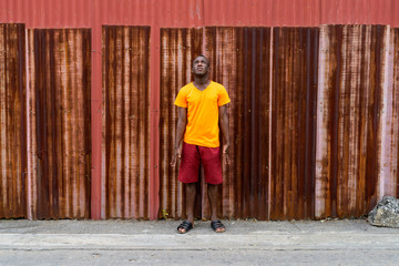 Young black African man standing while thinking and looking up a