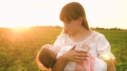 Fototapeta na wymiar Little baby is yawning in arms of young girl in glare of sunset. Young nanny walks with small kid.