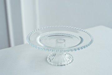The glass round stand is decorated with glass balls for cake and desserts on a white table on a white background.