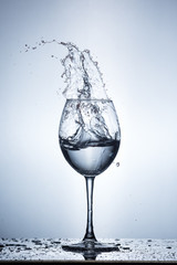 Splashing water on blue background. Wine glass with water.