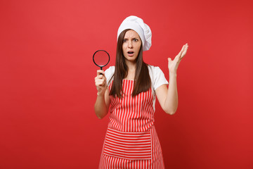 Housewife female chef cook or baker in striped apron white t-shirt toque chefs hat isolated on red wall background. Housekeeper woman hold and look through magnifying glass. Mock up copy space concept