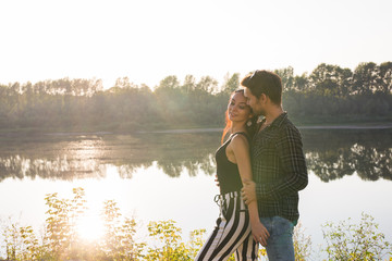 Romantic, love, people concept - young couple hugging near the lake at the sunset