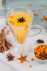 Two high glasses with colorful hot sea buckthorn tea with cinnamon sticks, anise stars and fresh sea buckthorn berries