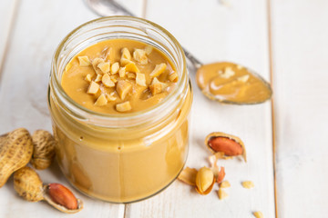 Peanut butter in glass jar, white wood background