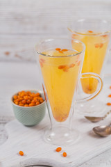 Two high glasses with colorful hot sea buckthorn tea with fresh sea buckthorn berries