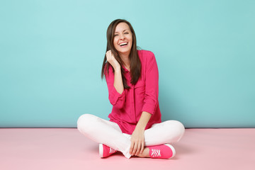 Full length portrait of smiling young woman in rose shirt blouse, white pants sitting on floor...