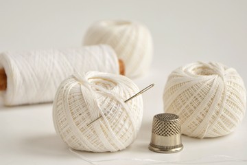 Fototapeta na wymiar Spools with white threads, needle and thimble on white background close-up.