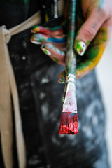Woman artist's hand with a brush and red paint. Black apron, white background.