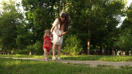 Naklejka na ściany i meble Mom and little daughter are walking along path in summer park. baby's first steps with mom