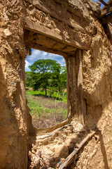 Ventana abierta de casa de barro en ruinas con arbol al fondo