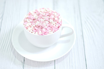 White coffee cup on wooden floor.Many small hearts, white and pink, are in a cup of coffee.Pink square wood with 1 and 4 white numbers, white glass..