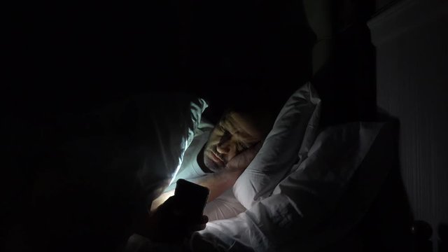 Man using his phone in his bed instead of sleeping, technology addiction concept