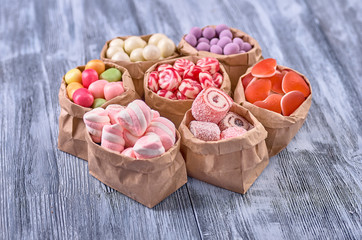 Colored candy in paper bags on wooden background