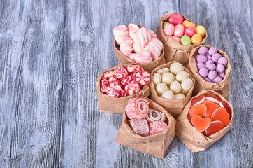 Colored candy in paper bags on wooden background