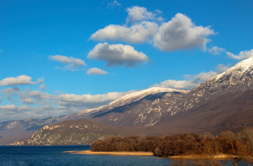 Fototapeta premium Winter landscape in Macedonia. Ohrid Lake and the picturesque hills of Galichitsa mountain under the blue sky with white clouds.