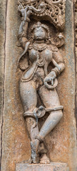 Belur, Karnataka, India - November 2, 2013: Brown wall stone panel sculpture of Shilabalika, celestial maiden, dancing with snakes outside temple wall. Damage by Muslim invaders.: face and vulva.