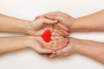 Close-up of the hand of an adult daughter and an older mother holding a heart together. Top view. Family and care concept