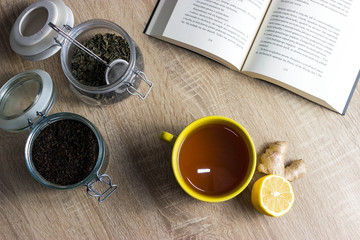 Obraz na płótnie Canvas Tea with lemon and book. In left corner black and green tea in jars