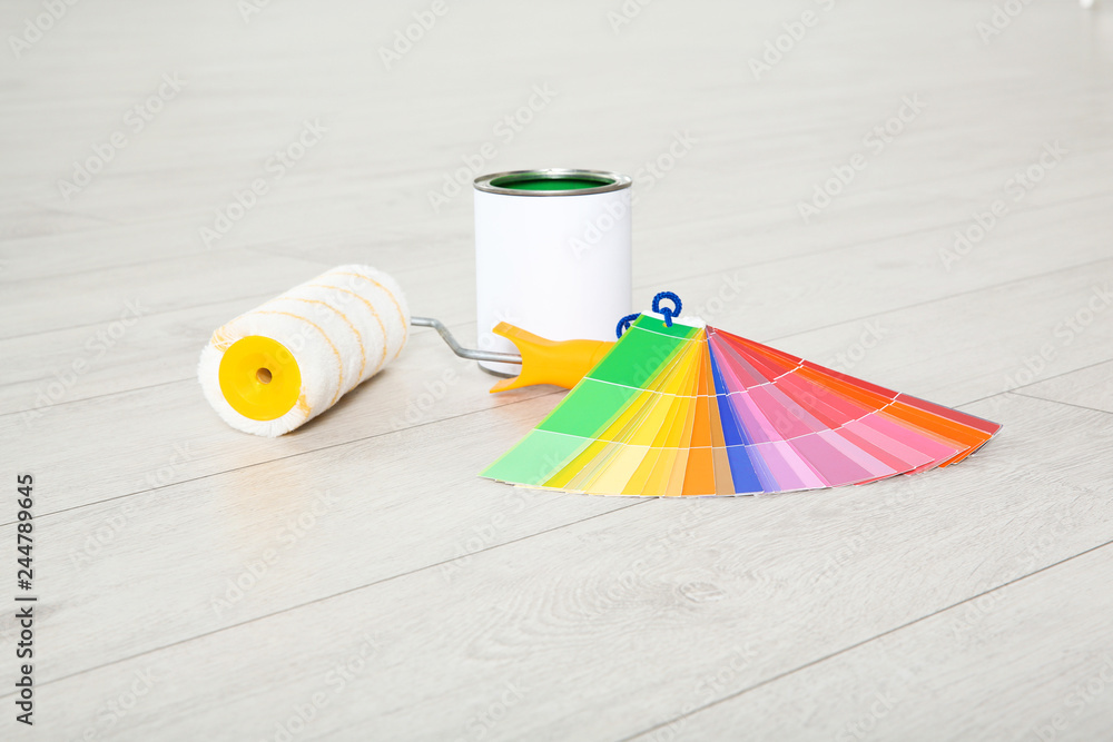 Wall mural Can of paint, roller brush and color palette on wooden floor indoors